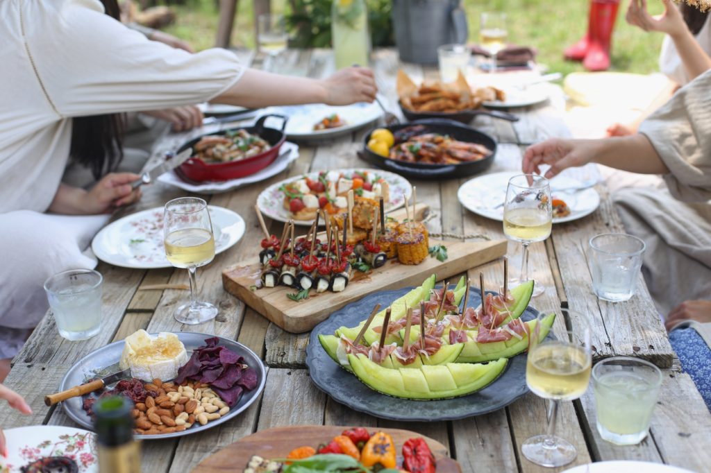 split expenses on group travel: a picnic table full of food and wine with hands reaching in