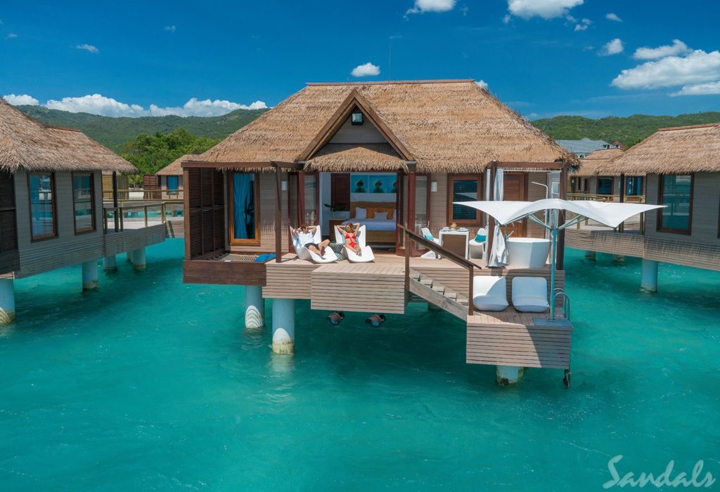 couple sits in loungers on the deck of a bungalow over the turquoise water- sandals south coast best swim up rooms in Jamaica 