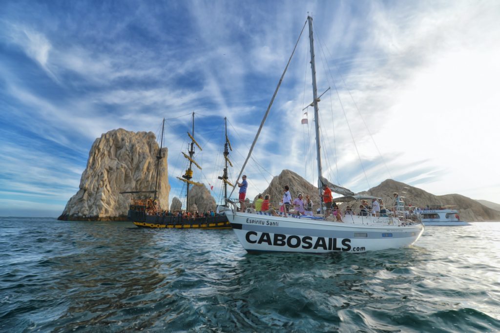 Cabo San Lucas, one of the fun places to go with friends, has sail boat tours on the water. A boat with people on it is at sea with rocks in the background