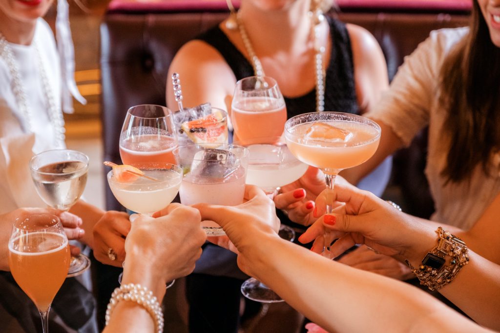 bachelorette party nyc with nine girls hands holding cocktails of different shapes and colors in for a cheers. cocktails are an integral part of all NYC itineraries