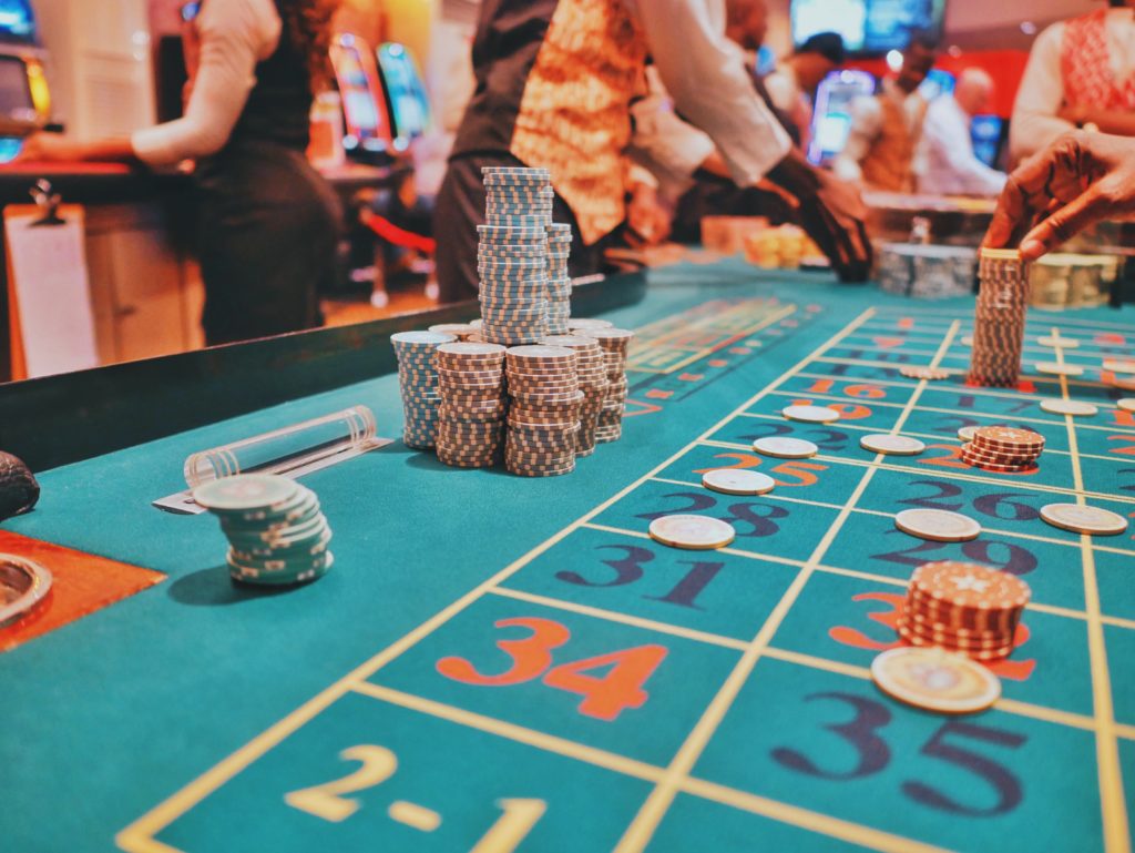 poker chips stacked on a roulette table with the dealers hands on one side and a player's hand stacking chips on the other