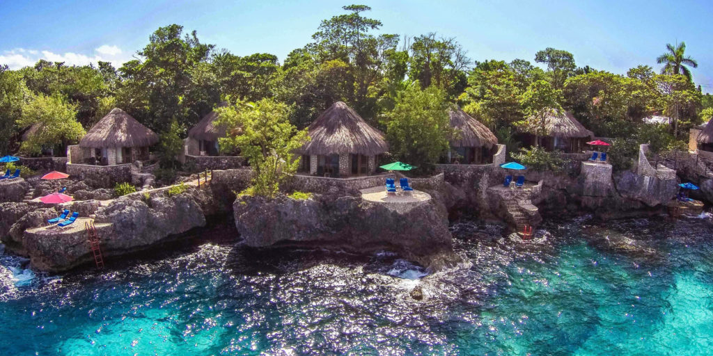 thatched roof stone cabanas sit on the edge of cliffs over bright turquoise Caribbean waters