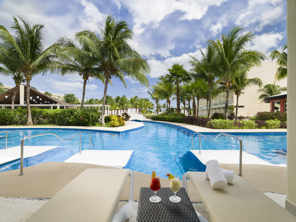 Two frozen tropical cocktails sit on a poolside table set between two white lounge chairs on the private patio of a swim up room at the Azul Beach Resort Riviera Cancun.