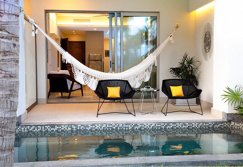 A white hammock hangs in front of sliding glass doors and behind two modern black chairs that sit on the private terrace of a swim up hotel room at the Garza Blanca Resort and Spa