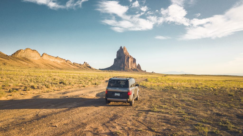 gray SUV driving on a dirt path through grassy flatlands with rock formations in the distance