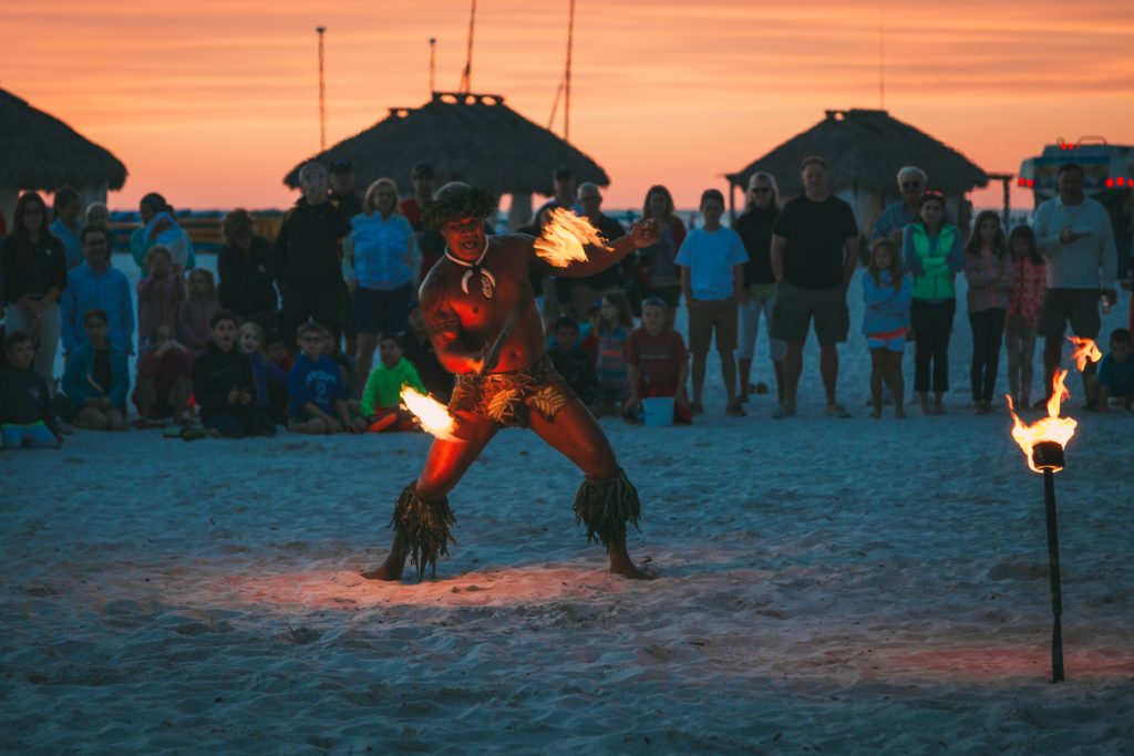 50th Birthday Trip Ideas: Florida. Man spinning fire on the beach at sunset with tourists watching in the background 