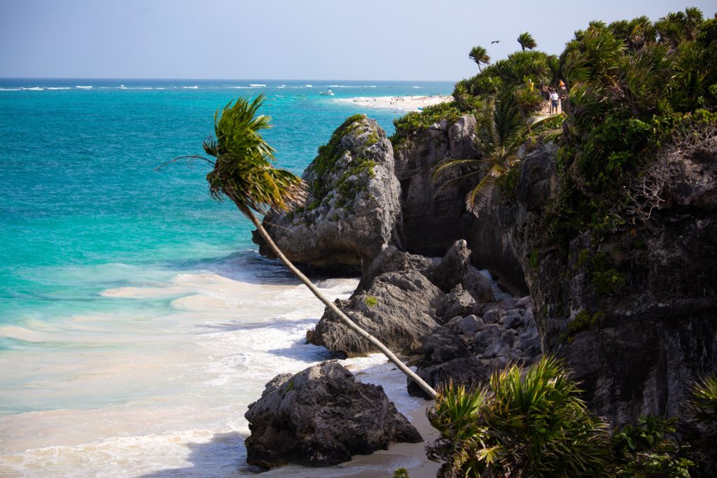 bright blue water and white sand by palm tree covered cliffs in Tulum
