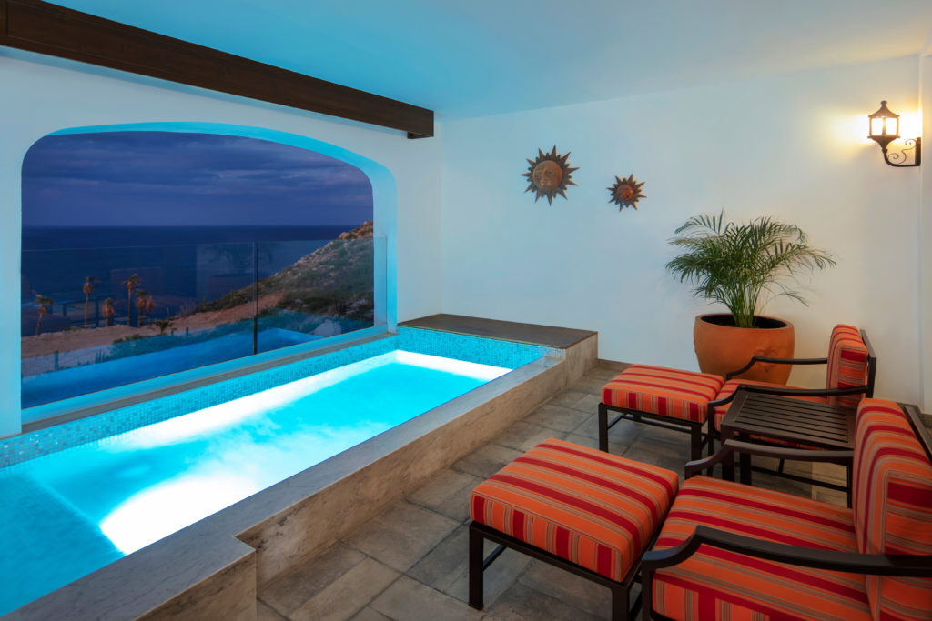 Beautifully lit up plunge pool on a balcony with orange chairs and a view overlooking the beach. Vista Encantada resort is one of the best places to stay in Cabo San Lucas.