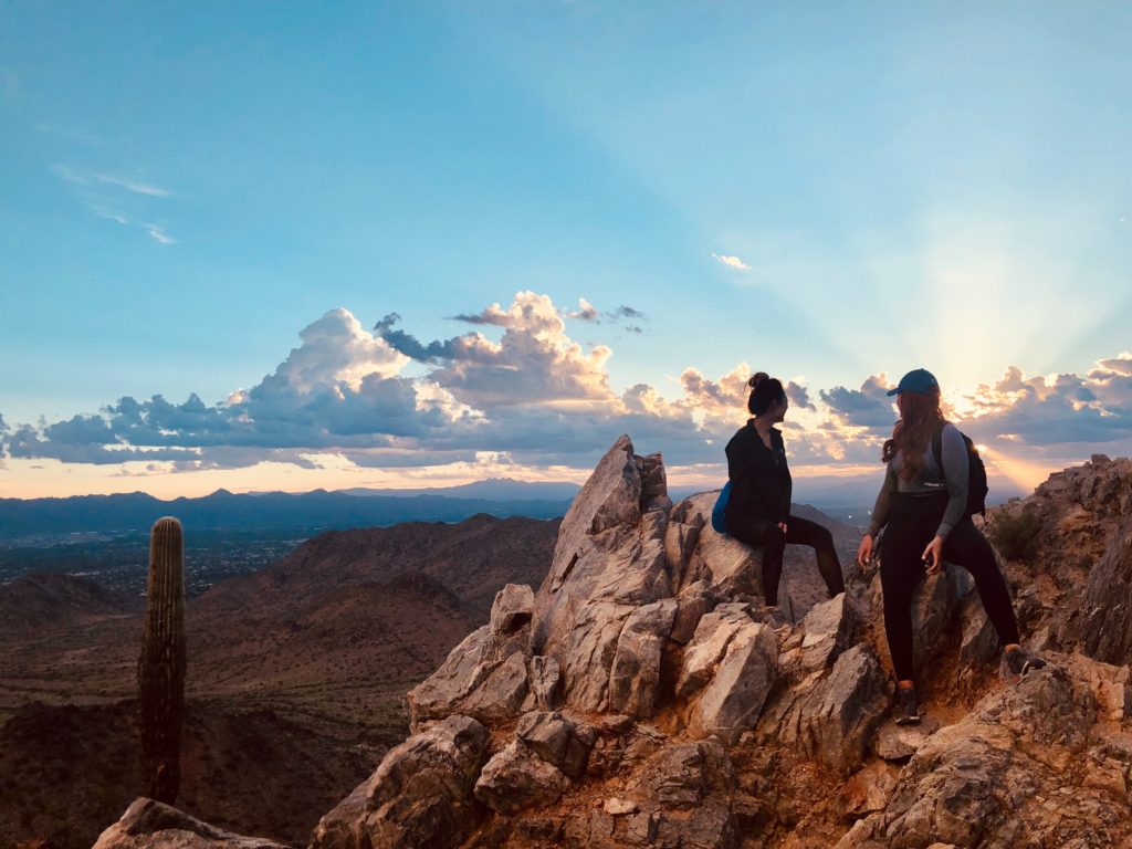 scottsdale bachelorette hiking. 2 girls sit on jagged rocks looking out over the desert and sunset
